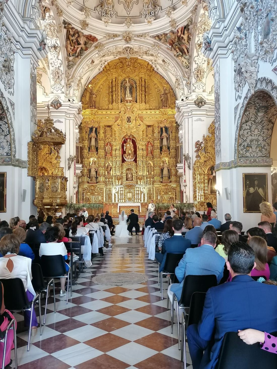 Interior de un templo barroco con retablo dorado durante una boda